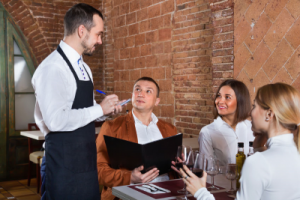 A waiter in a restaurant receives orders from customers at a table