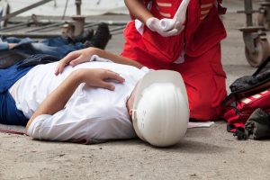 A person in a white hard hat lying on the floor and receiving medical treatment.