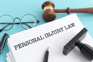 'Personal injury law' written on a piece of paper next to a gavel and pair of glasses on a desk. 