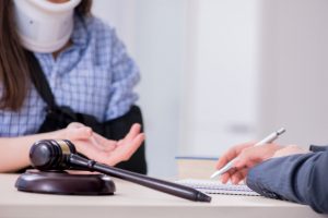 A person wearing a neck brace with their left arm in a sling. They are talking to their solicitor, who is holding a pen.