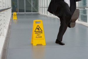 A business man slips on a wet floor beside a yellow wet floor sign