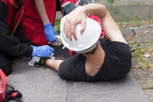 Man In Hard Hat Being Treated On The Scene Following An Accident At Work. 