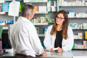 A female pharmacist dispensing medicines to a male patient behind the pharmacy counter.