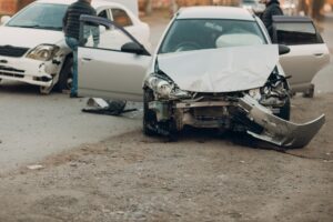 A driver gets out of an open car door. The front of the car is destroyed.