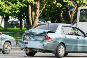 A blue car sits in the road with a damaged back fender