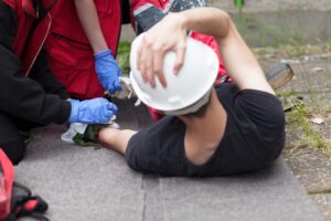 An injured man in a white hardhat clutches his head in pain