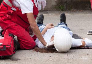A woman in a white hardhat lies unconcious on the ground