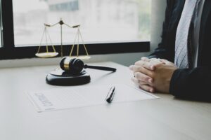 A Solicitor's Folded Hands On A Desk Next To A Gavel And Pen.