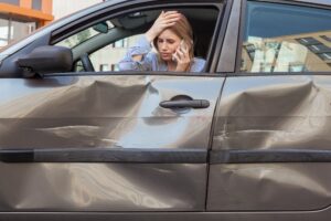 Woman In A Dented Car Talks On The Phone. 