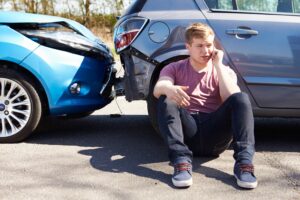 Man Sits On Floor With Phone In Front Of Rear End Car Accident. 