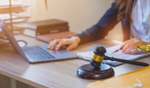 A Trained Legal Advisor Sits At A Table With A Hand On A Laptop Next To A Gavel. 