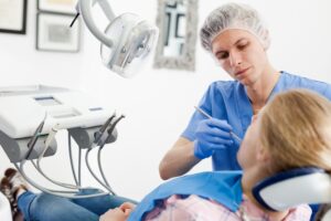 A young woman in a dentist chair with a young male dentist doing a dental check-up. 