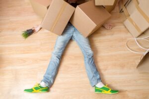 A man laying on the floor under a pile of boxes after an office accident.