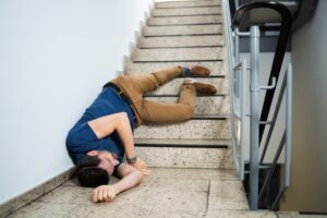 A man laying unconscious at the bottom of a staircase after slipping due to no wet floor signs being displayed