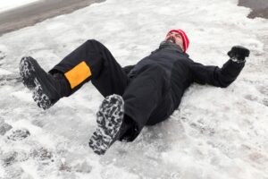 A man in a bright orange hat slips and falls on ice