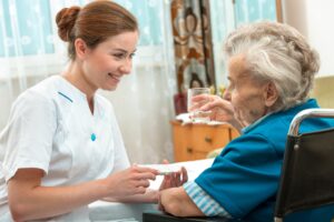 A friendly female home carer giving medication to an elderly woman in a wheelchair wearing a blue t-shirt.