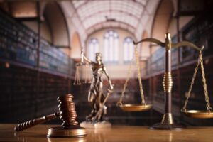 An empty courtroom with a gavel, scales and statue in the forefront of the picture. 