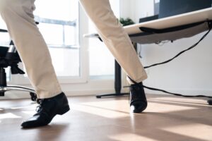 A man in khaki pants trips over a loose wire in an office. 