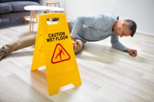 An older man in a business shirt lays injured on the ground after slipping on a wet floor