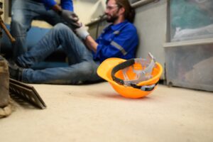 A factory worker on the floor with an injured hand due to a breach of health and safety laws.