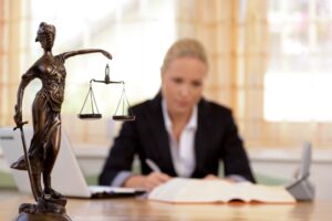 An anaesthetic negligence claim solicitor sitting at a desk and writing. A statue of the scales of justice sits in the foreground.