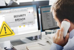 An employee making a phone call while looking at a computer screen that has the words 'security breach' in large text on it.