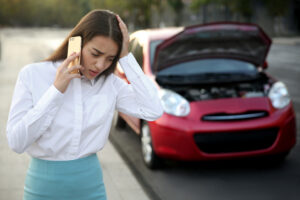A distressed woman talks on the phone near to a damaged car on the road.