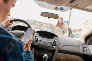 An image shows distracted driving as a driver looks at their phone whilst about to hit a pedestrian. 