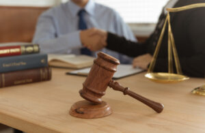 A medical data breach claim solicitor shaking hands with a client. There is a set of justice scales and a gavel on the desk.