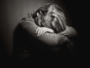 A black and white image of a woman with her head in her folded arms looking distressed