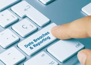 A finger presses down on a white computer key with the words 'data breaches and reporting' on it.
