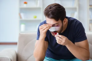 A man with a bloody bandaged nose sat at home holding his forehead